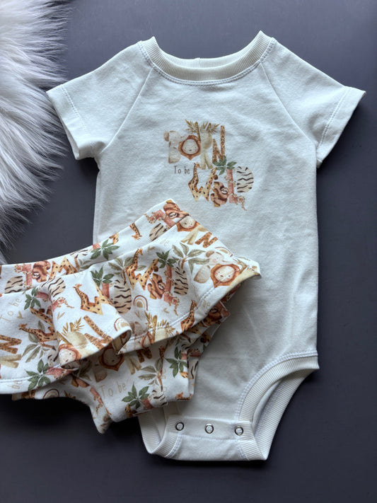 White baby onesie with animal print and matching skirted bummies on a dark surface