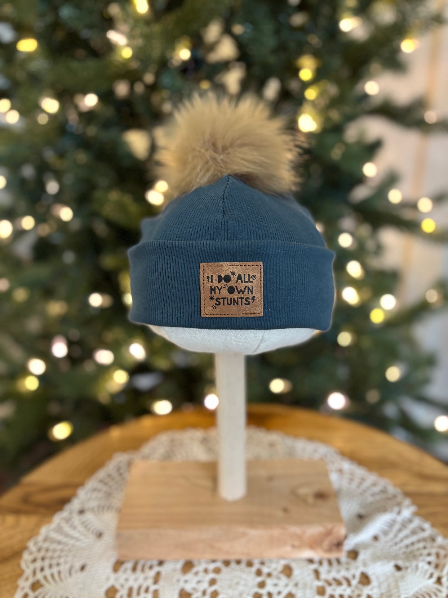 Blue beanie with pom-pom on a mannequin head in front of a decorated Christmas tree.