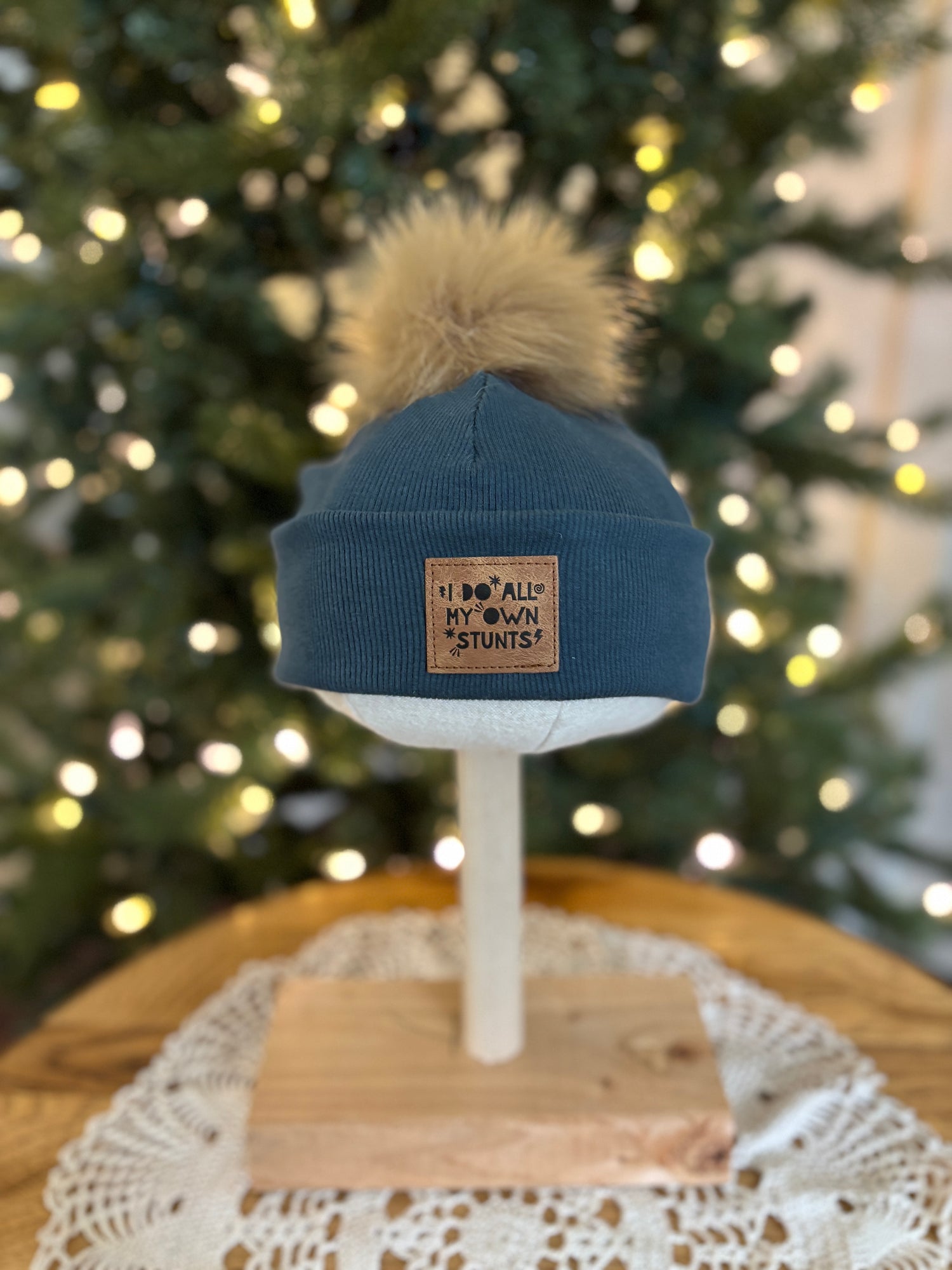 Blue beanie with pom-pom on a mannequin head in front of a decorated Christmas tree.