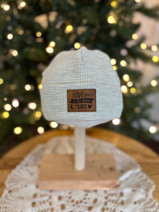White cap on a mannequin head with a leather patch in front of a decorated Christmas tree.