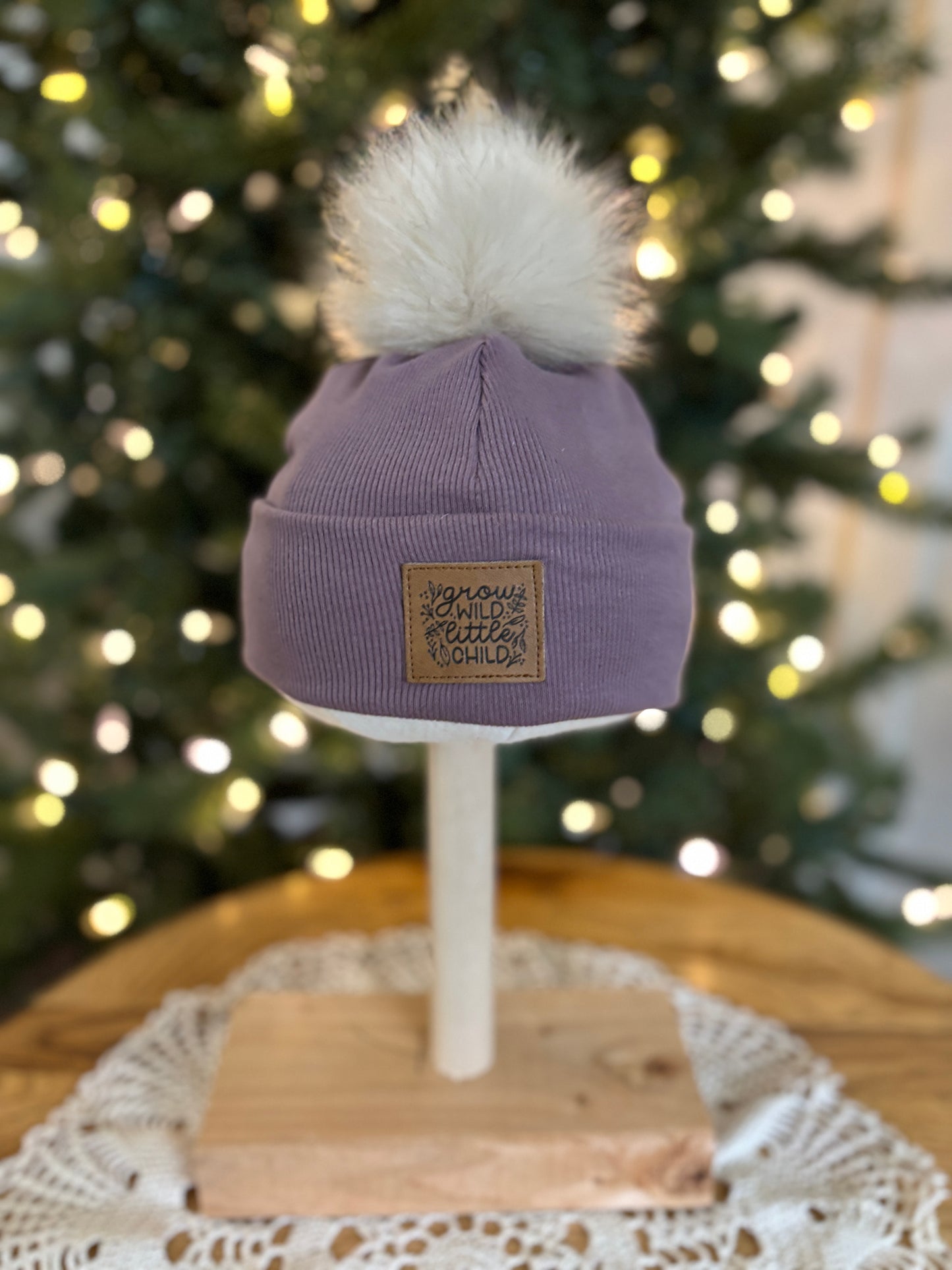 Purple beanie with pom-pom on a mannequin head against a Christmas tree background