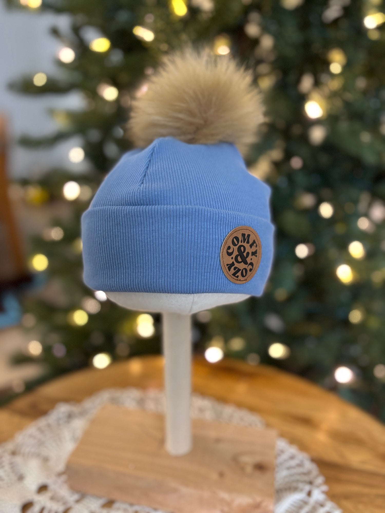 Blue beanie with a pom-pom on a mannequin head against a blurred Christmas tree background
