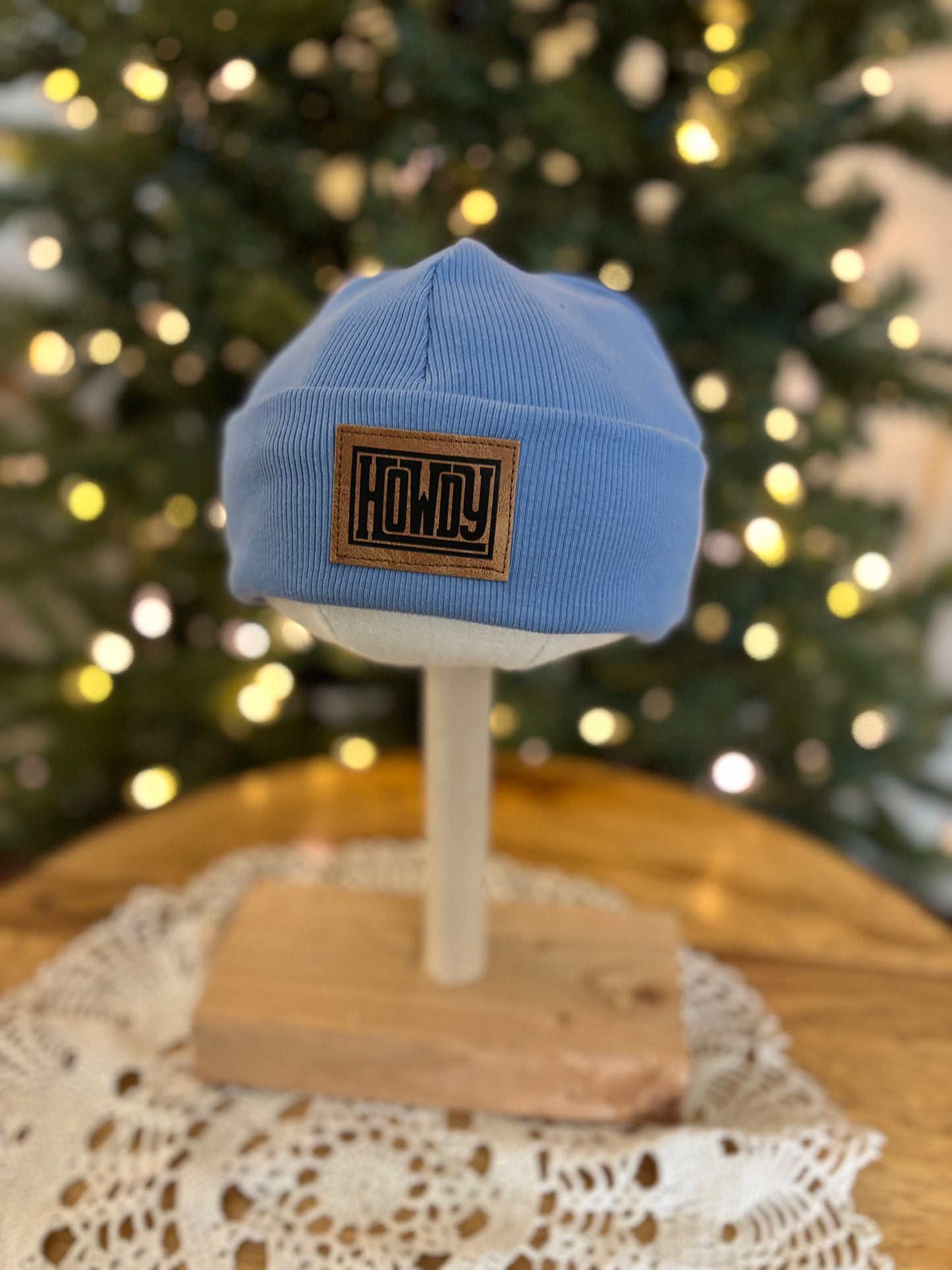 Blue beanie with a patch on a mannequin head in front of a decorated Christmas tree.