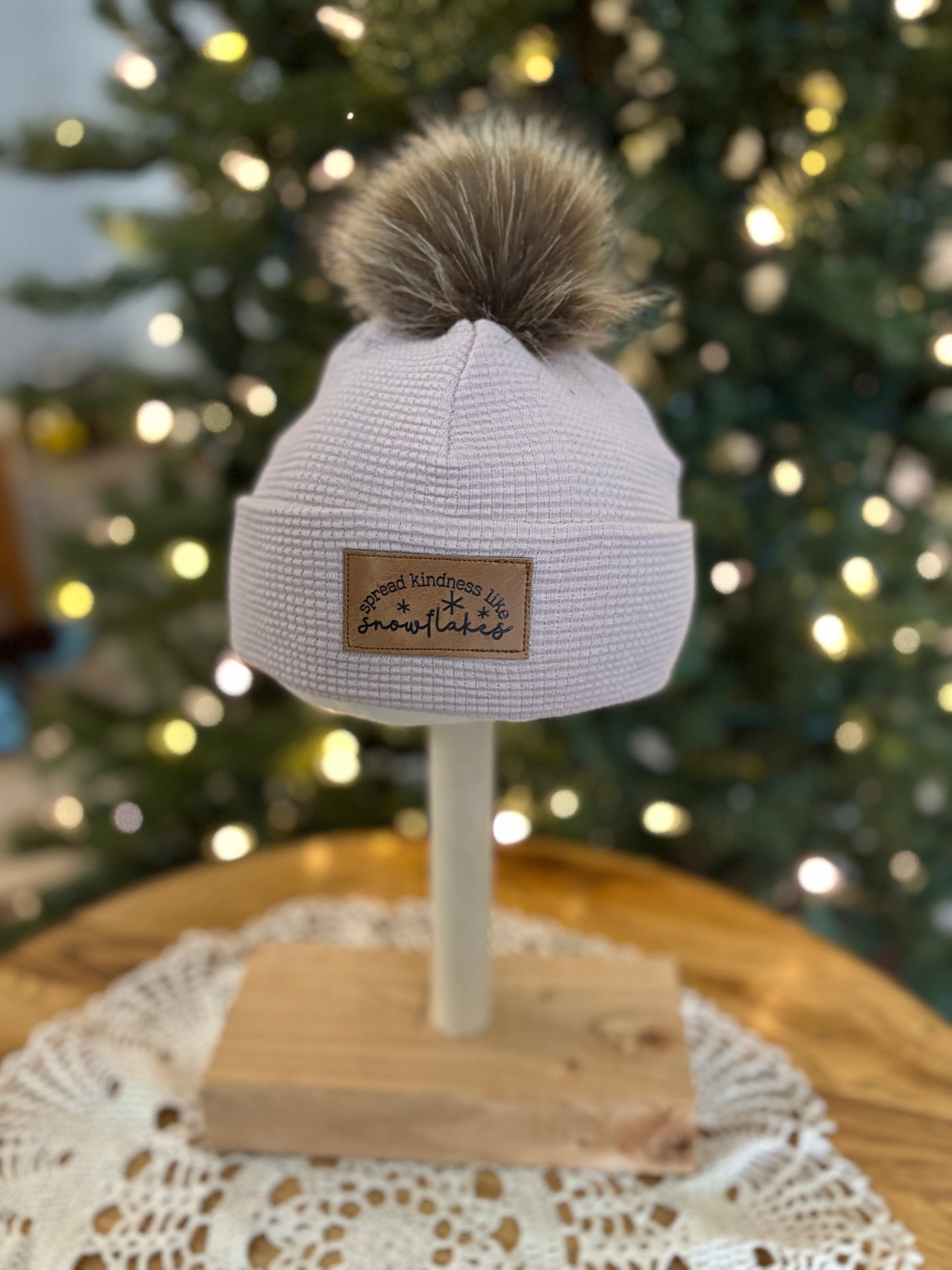 White knit beanie with pom-pom on a mannequin head against a blurred Christmas tree background.