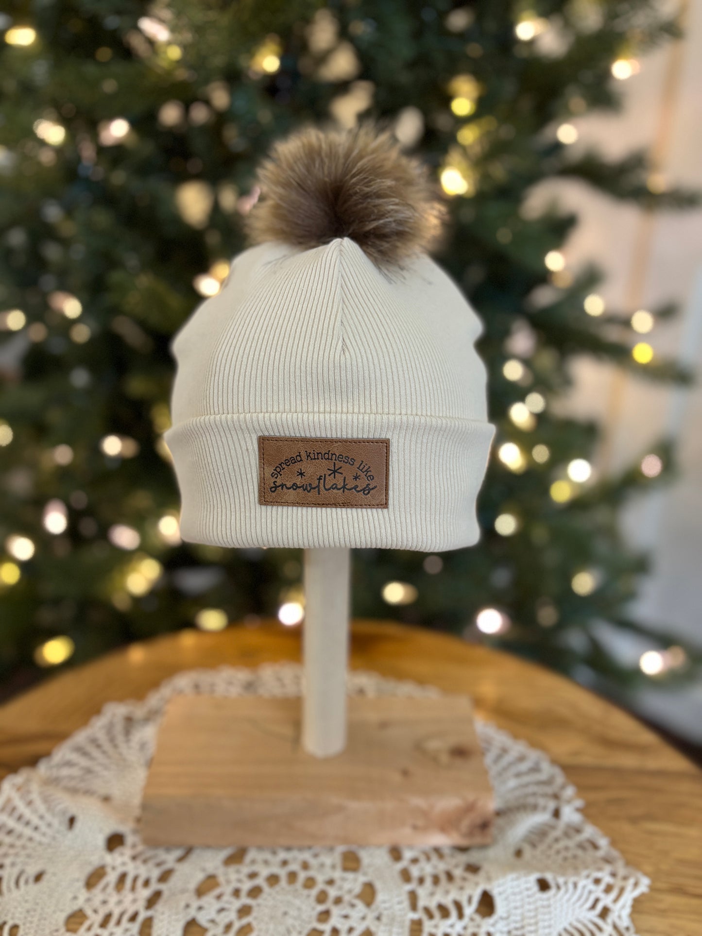 White beanie with brown pom-pom on a mannequin head in front of a decorated Christmas tree.