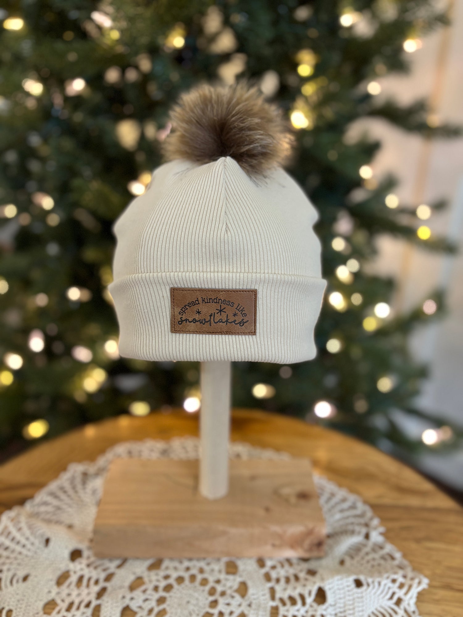 White beanie with brown pom-pom on a mannequin head in front of a decorated Christmas tree.