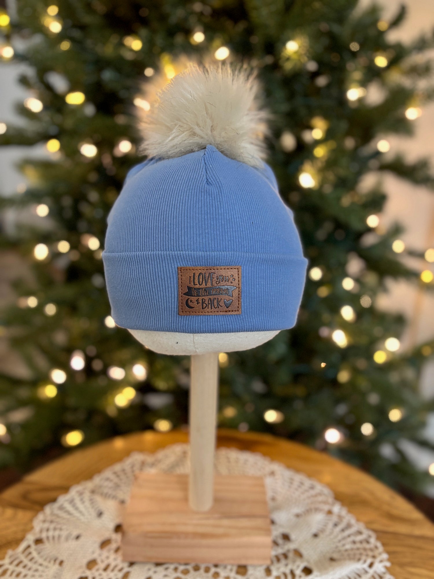 Blue beanie with a pom-pom on a mannequin head in front of a decorated Christmas tree.