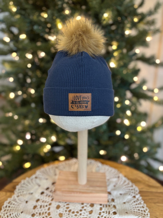 Blue beanie with pom-pom on a mannequin head in front of a decorated Christmas tree.