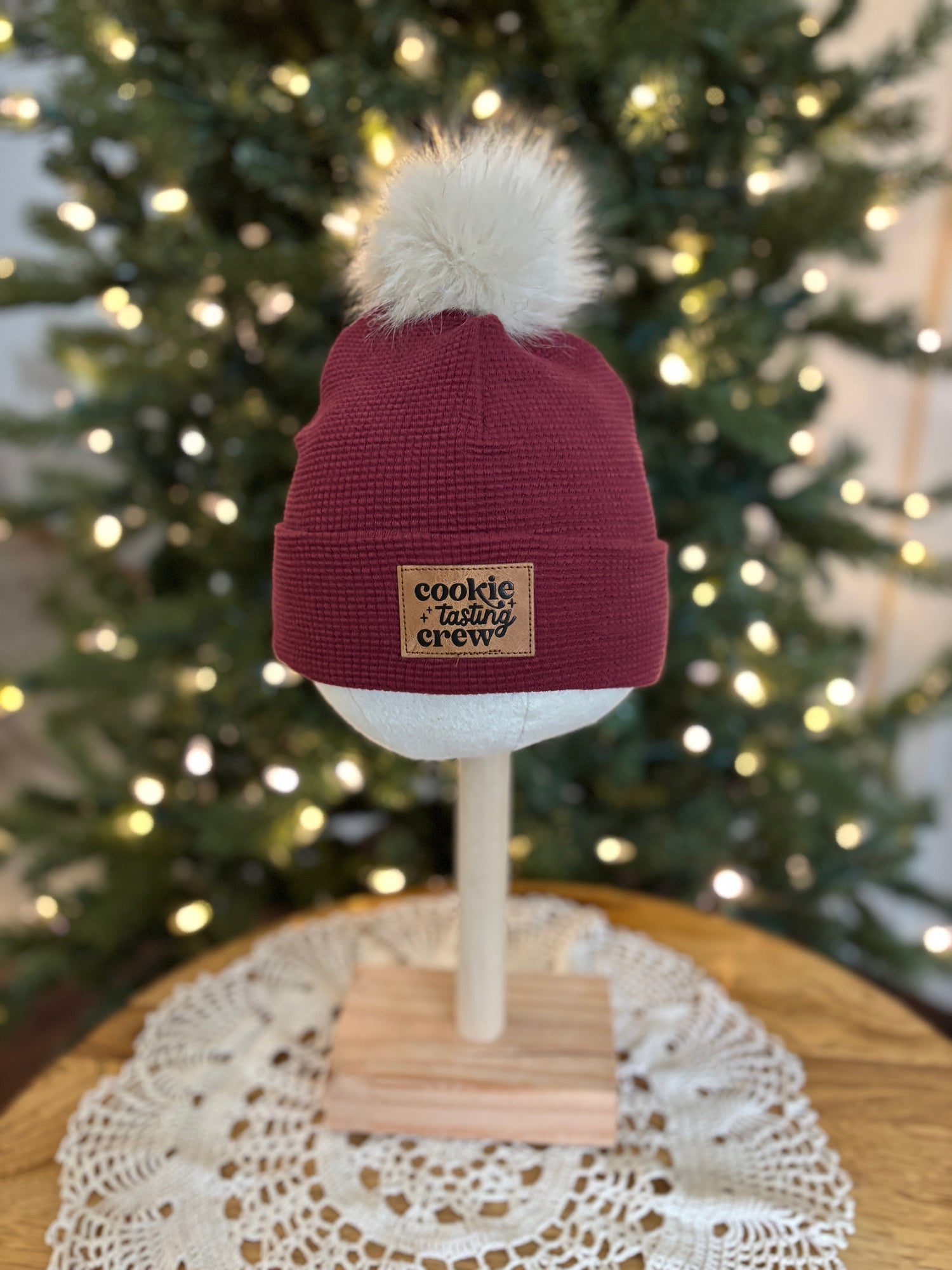 Maroon beanie with white pom-pom on a mannequin head in front of a decorated Christmas tree.