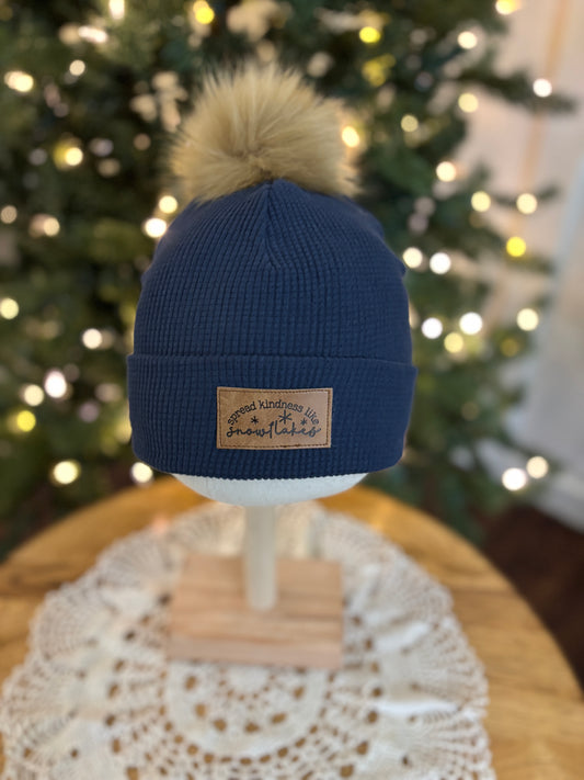 Blue beanie with a pom-pom on a mannequin head against a blurred Christmas tree background