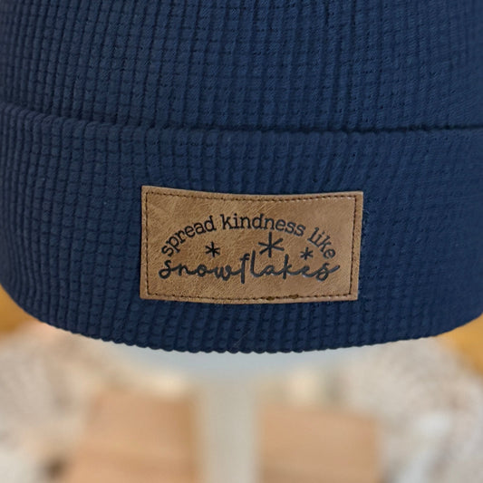 Blue beanie with a pom-pom on a mannequin head in front of a Christmas tree.