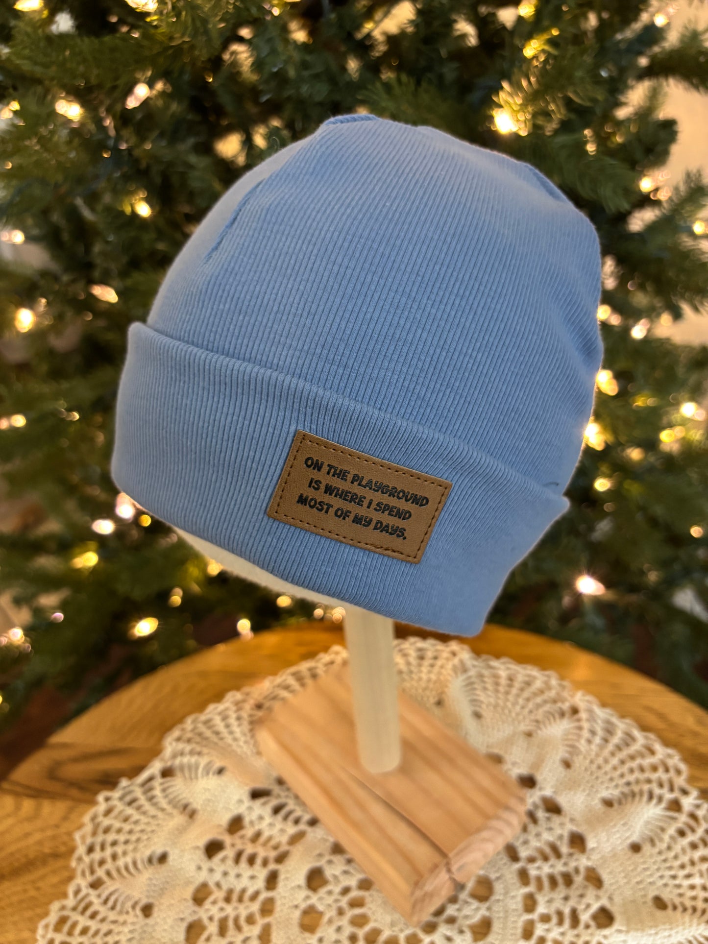 Blue beanie with a brand label on a wooden surface with a blurred Christmas tree background