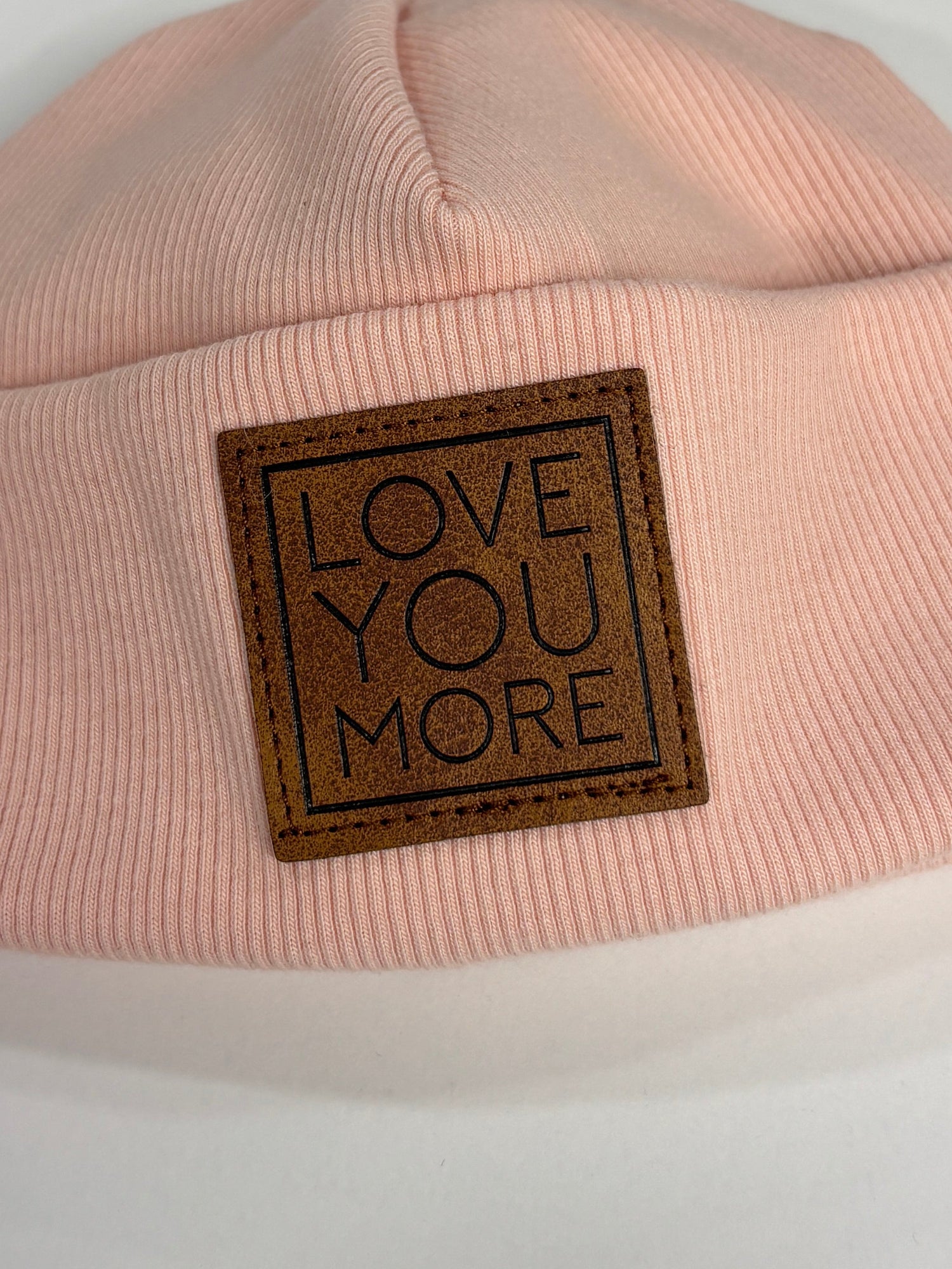 Pink beanie with 'LOVE YOU MORE' label on a white background