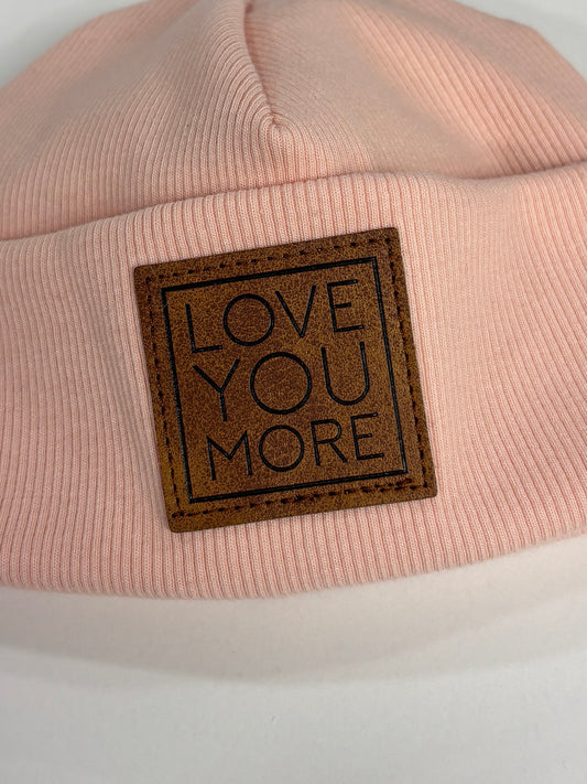 Pink beanie with 'LOVE YOU MORE' label on a white background