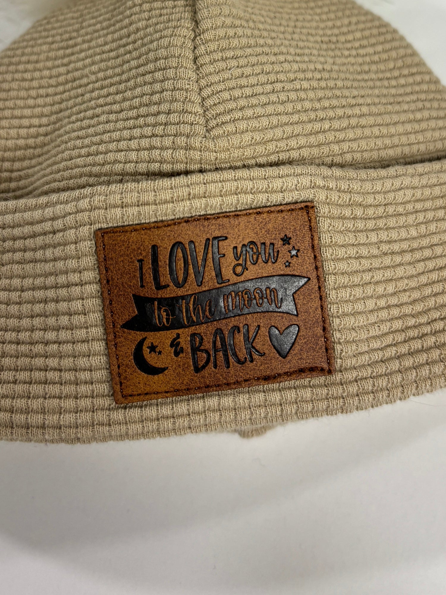 Beige knit beanie with a fur pom-pom and leather patch on a white background