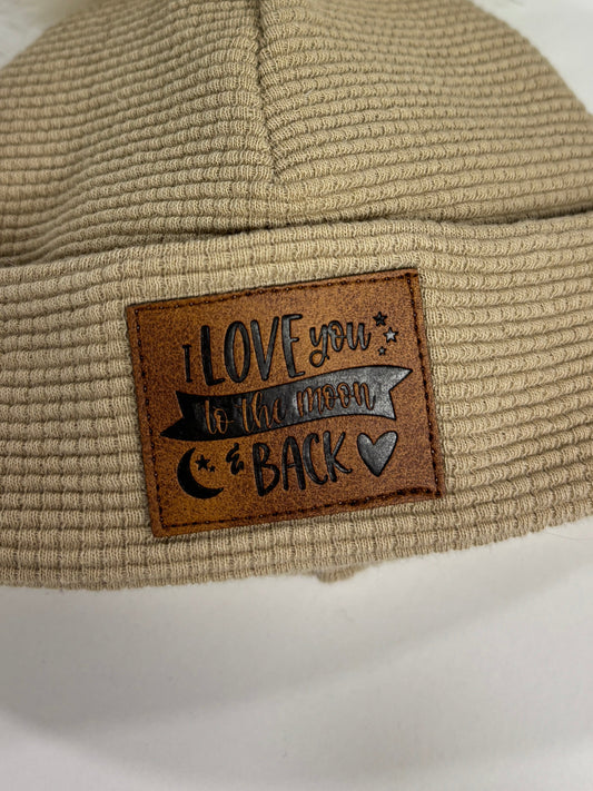 Beige knit beanie with a fur pom-pom and leather patch on a white background