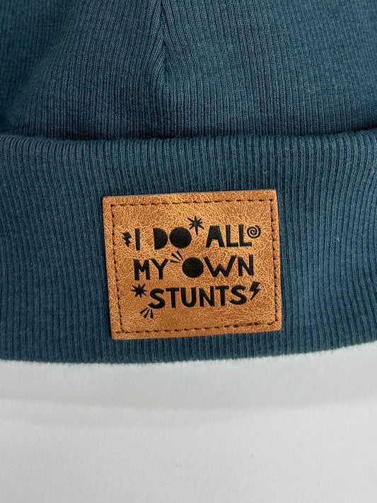 Blue beanie with a fur pom-pom and leather patch on a white background