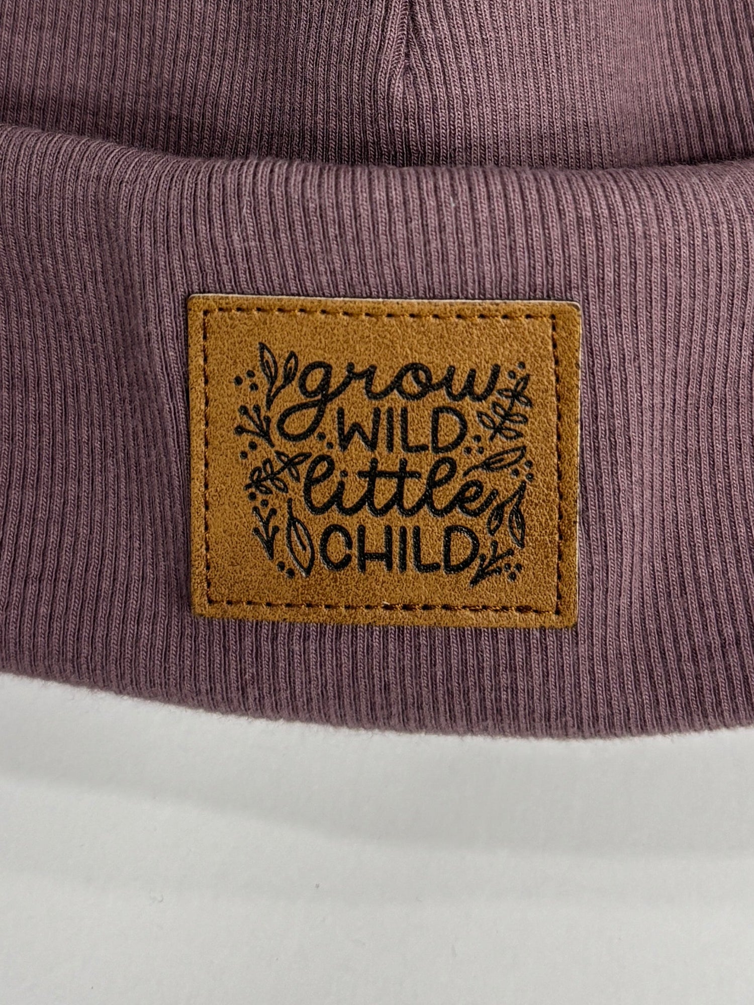 Purple beanie with fur pom-pom and leather patch on a white background