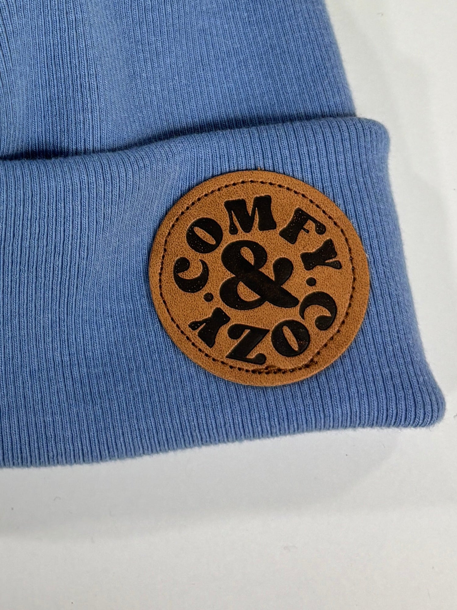 Blue beanie with a brown pom-pom and logo on a white background