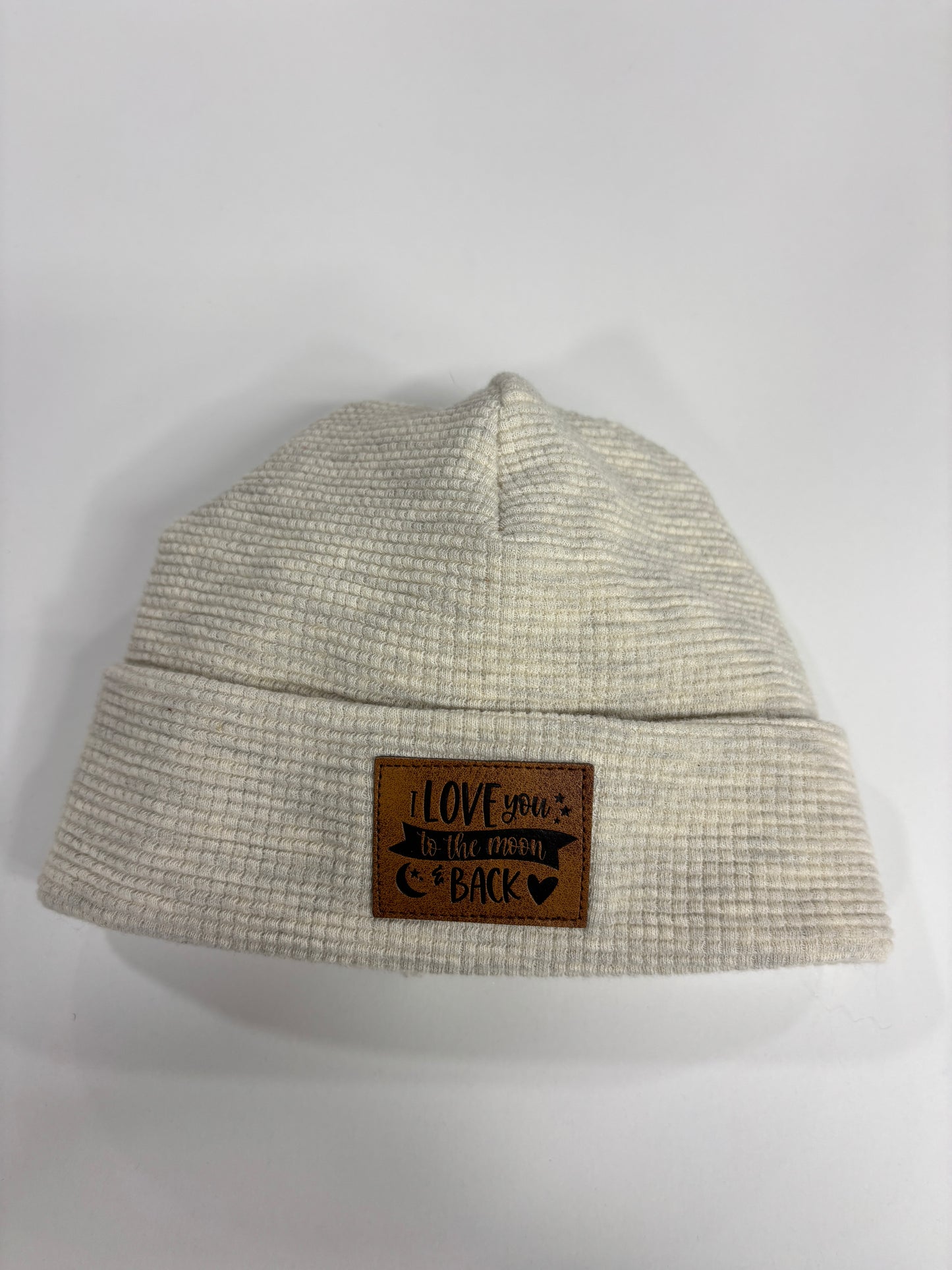 Beige textured beanie with a brown leather patch on a white background