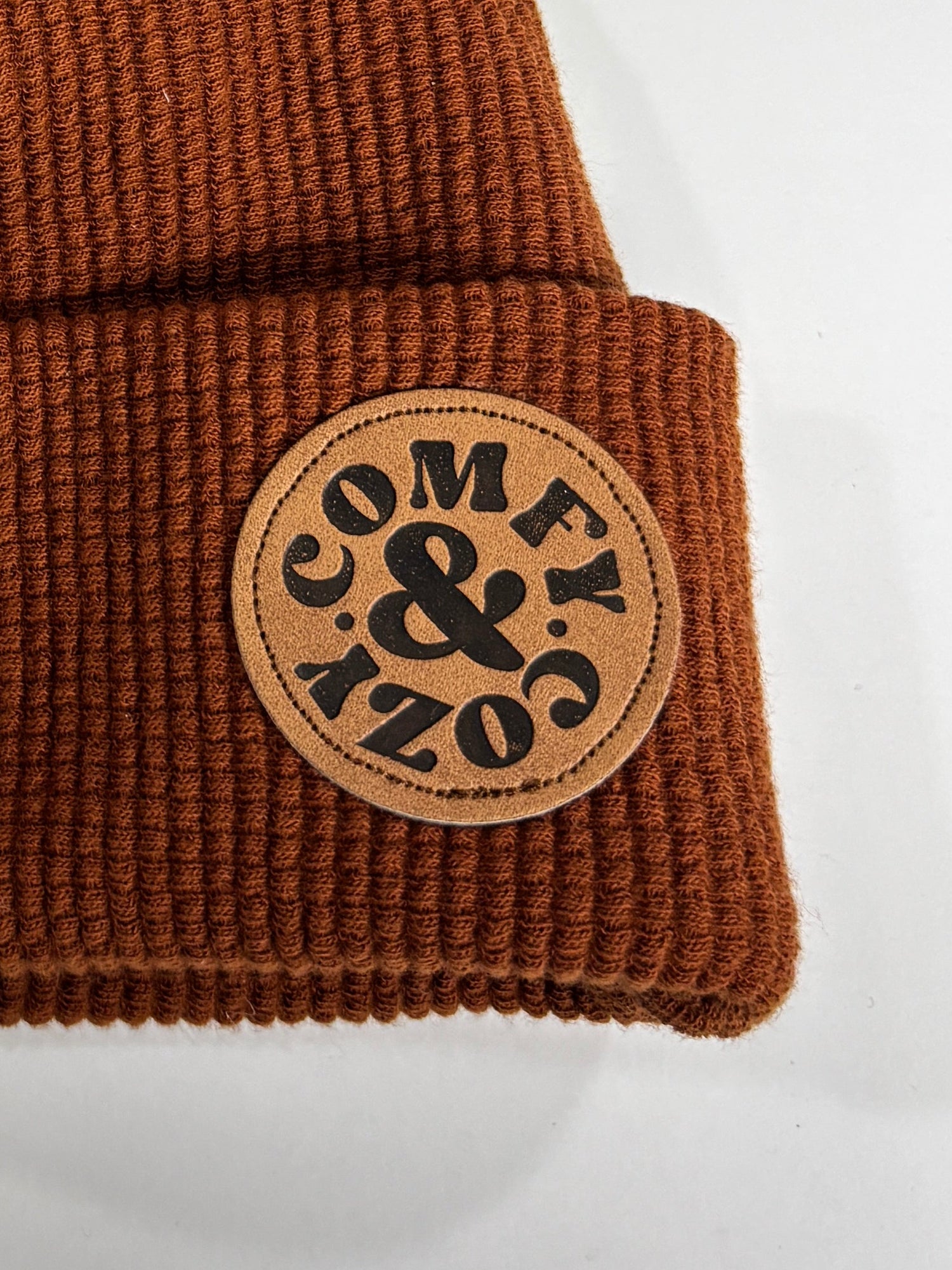 Brown knit beanie with pom-pom and logo on a white background