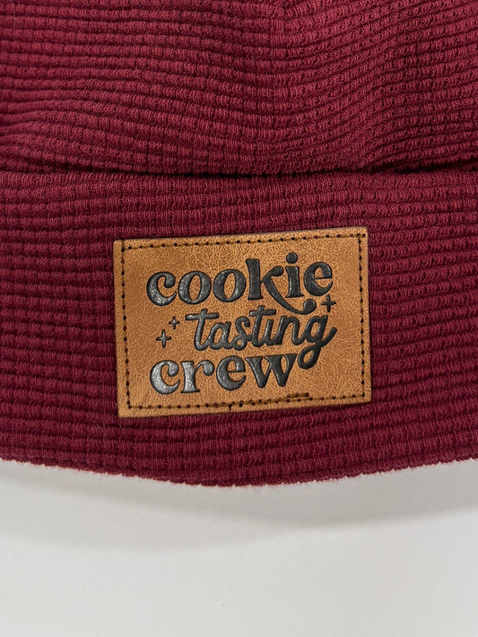 Maroon knit beanie with a fur pom-pom and brand label on a white background
