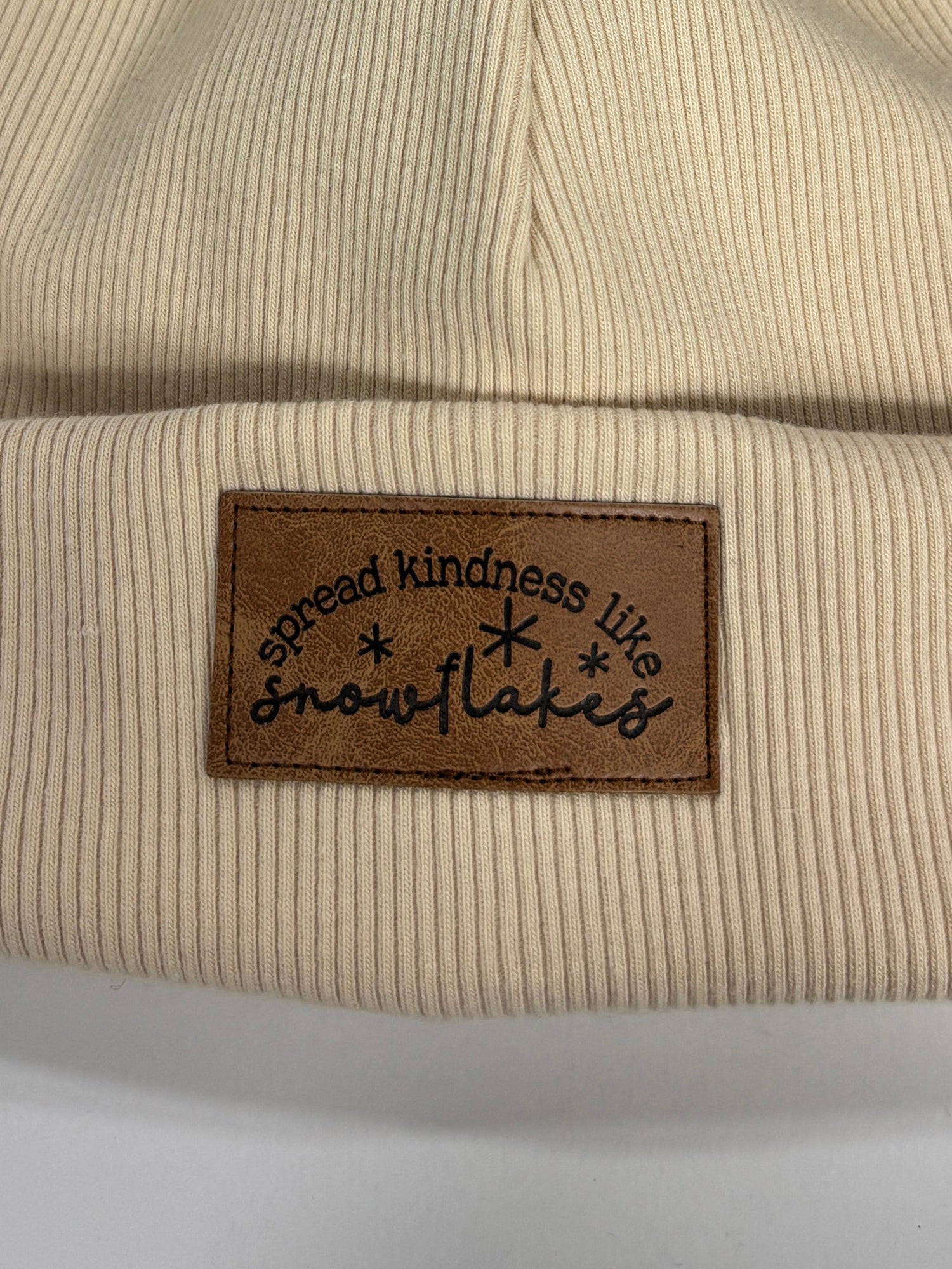 Beige beanie with fur pom-pom and brand label on a white background